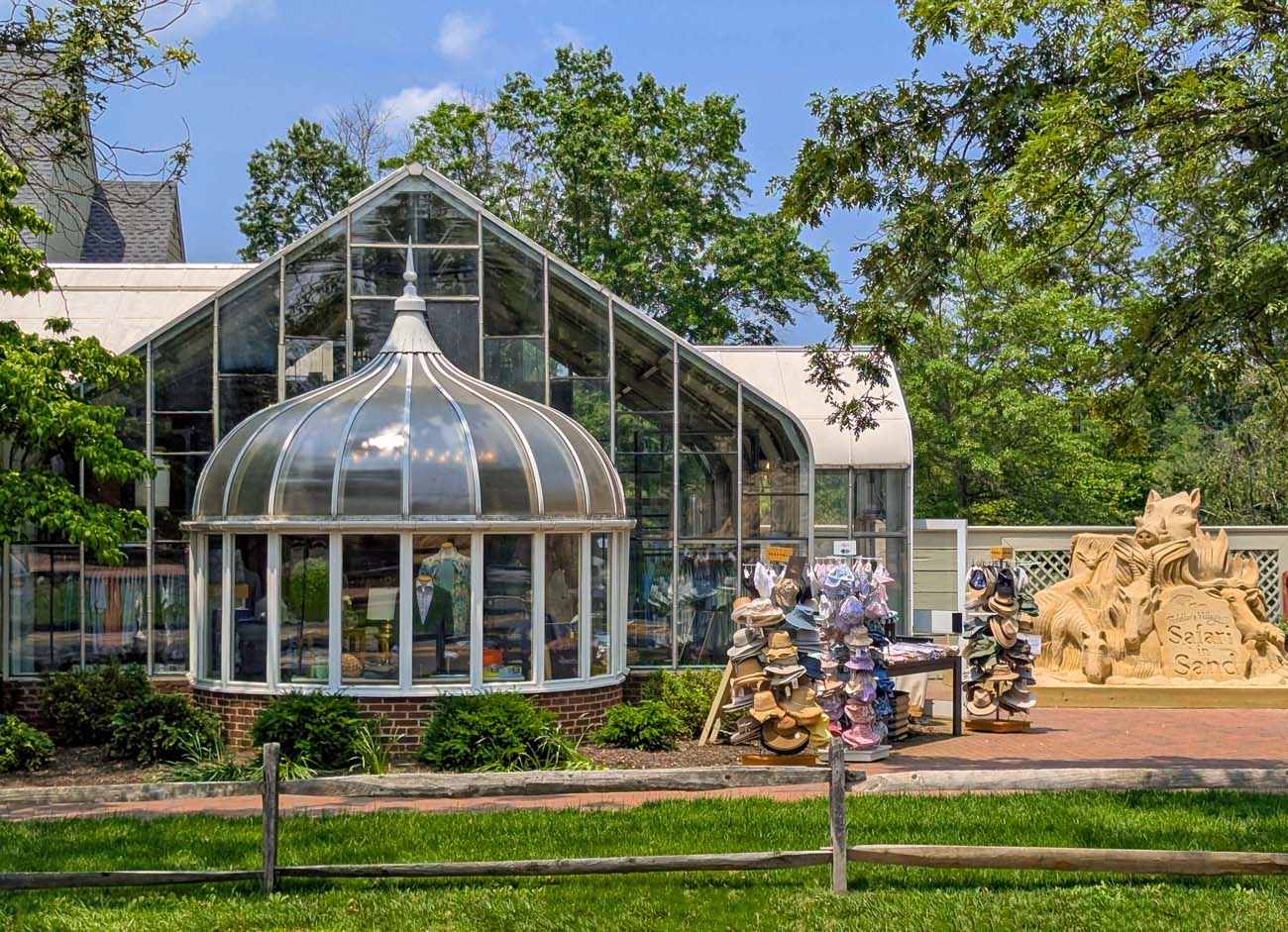 Distinctive domed section and peaked roof at Fox and Holly surrounded by lush green lawns and mature trees, with Safari in Sand sculpture visible in foreground featuring carved safari animals