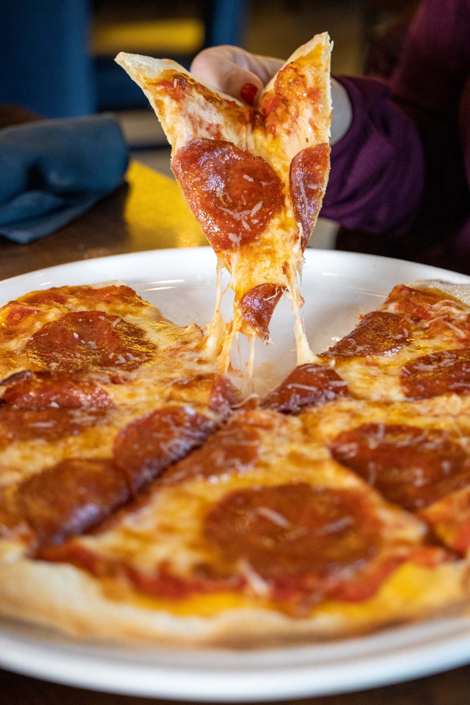 A cheese pull shot of a pepperoni pizza showing melted mozzarella stretching from a lifted slice, with perfectly crispy pepperoni cups