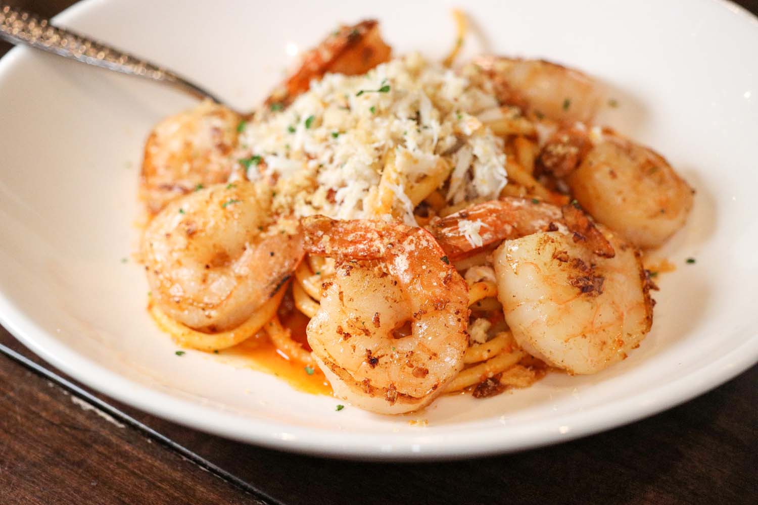 Close-up of perfectly seared jumbo shrimp atop bucatini pasta in a spicy calabrian vodka sauce, garnished with freshly grated parmesan cheese and chopped parsley on a white ceramic plate