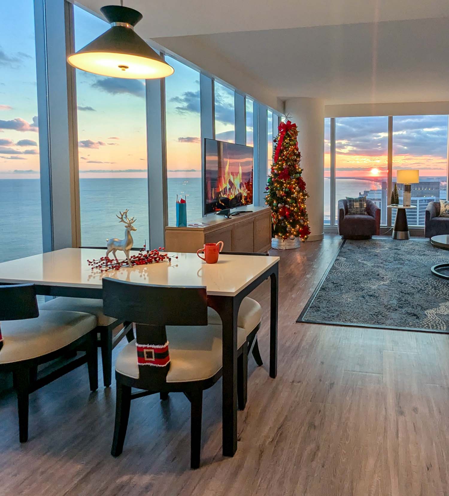 Dining area in hotel suite with white table, black chairs, ocean view windows, Christmas tree, and holiday decorations including reindeer figurine and Santa chair cover