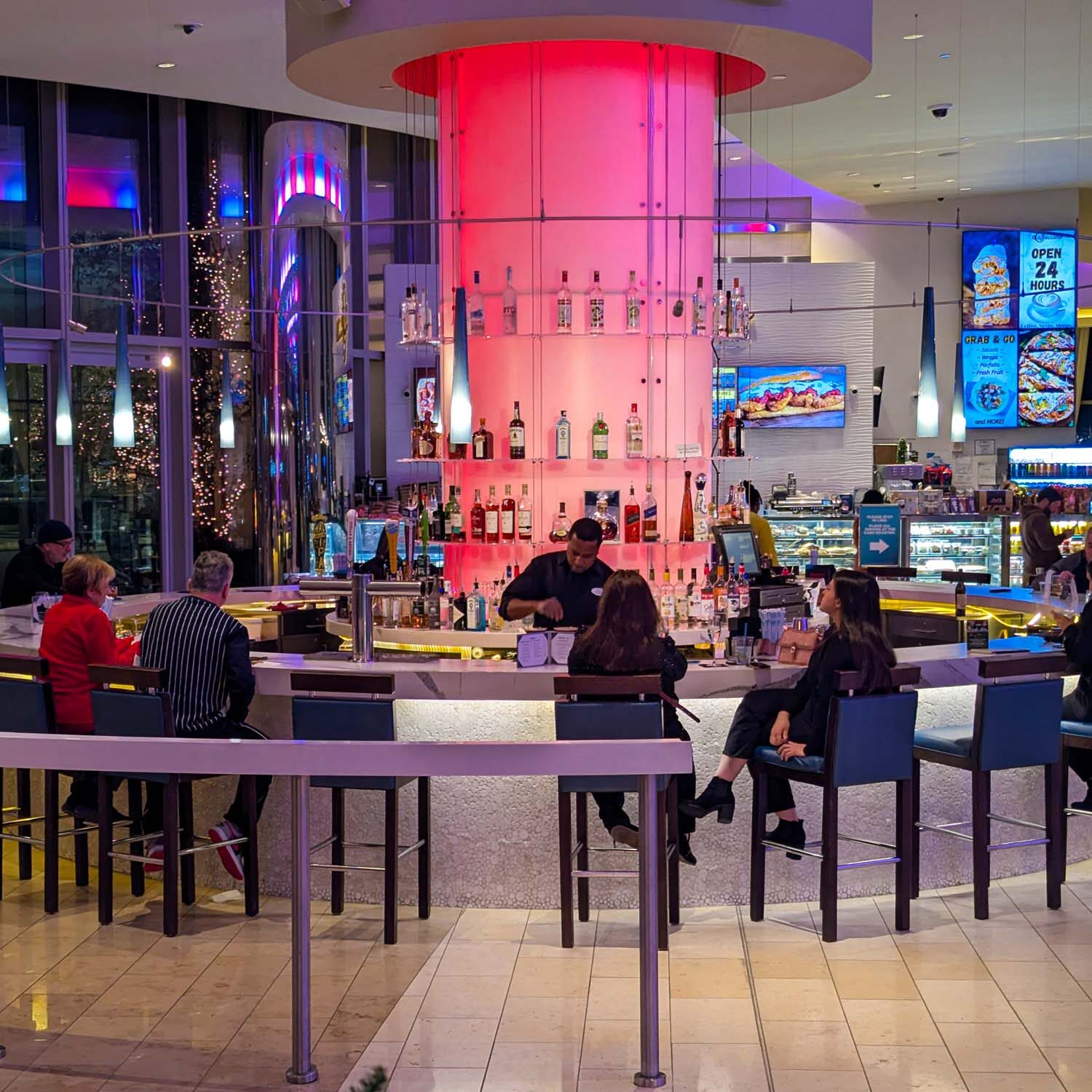 Modern circular bar with pink LED lighting, liquor display, and holiday greenery featuring blue lights in the foreground