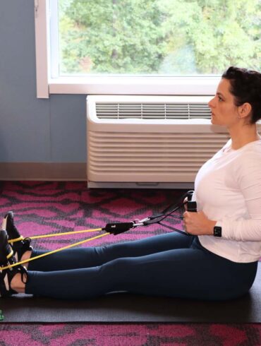 Woman performing seated resistance band rows in home or hotel setting, demonstrating Future app's flexibility for maintaining fitness routines while traveling
