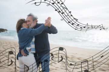 An older couple dances together joyfully on a beach, holding hands in a classic dance position. The man with gray hair and beard wears a dark blue sweater and jeans, while the woman in a blue cardigan and white pants leans in closely. They're smiling warmly at each other as they dance on the sand with the ocean visible in the background. Decorative musical notes and staff lines flow around them, symbolizing the rhythmic nature of dance. This image perfectly illustrates how dance combines physical activity, social connection, and joy—key elements discussed in the article about dancing's superior benefits for cognitive health and emotional wellbeing across the lifespan.