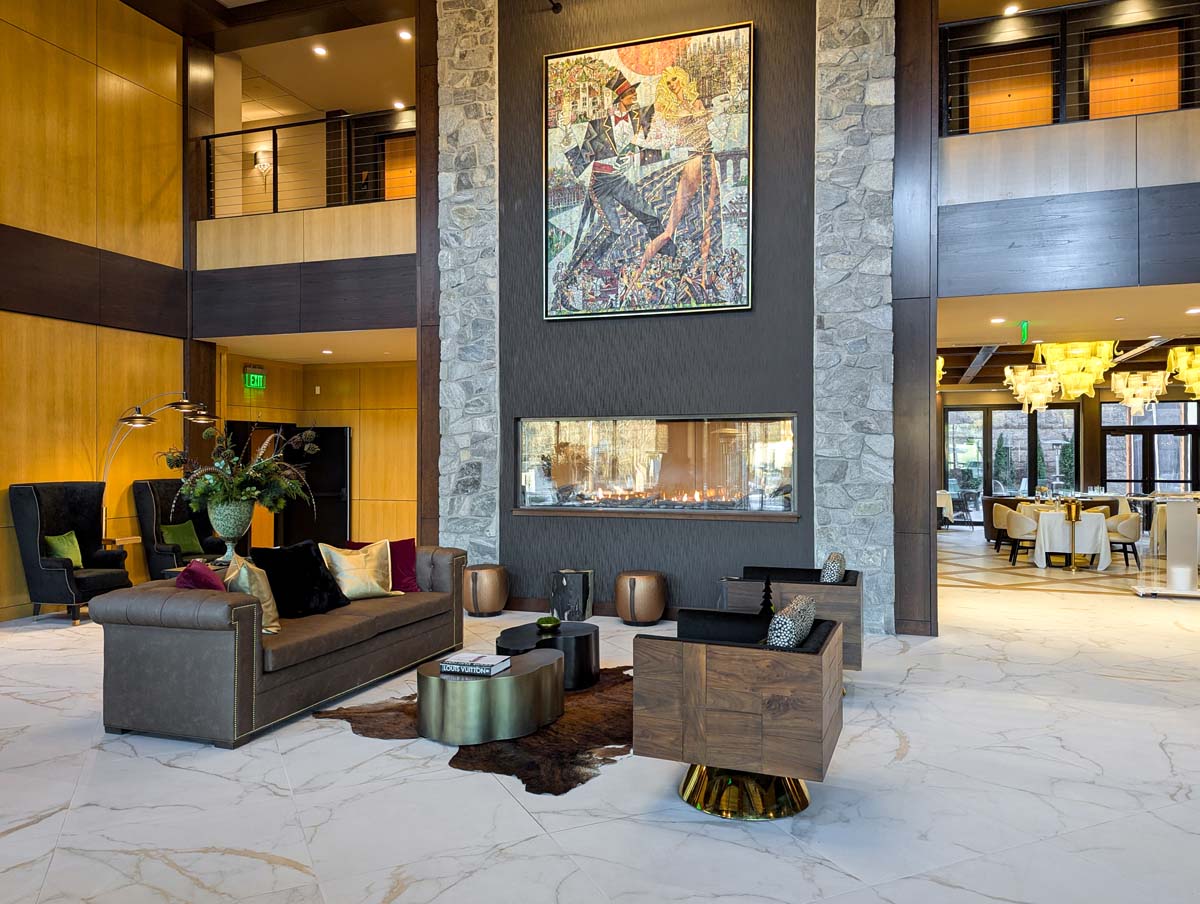 Modern hotel lobby with two-story stone fireplace, contemporary artwork, marble floors, and sophisticated seating areas