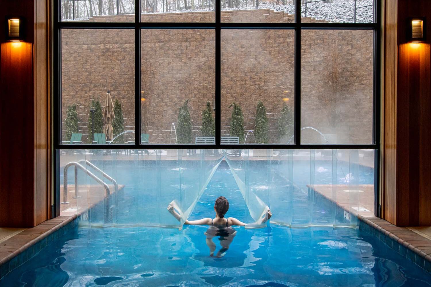 Heather from Better Living enjoying the heated indoor outdoor pool at The Swiftwater. Arching water features while snow falls outside the floor-to-ceiling windows