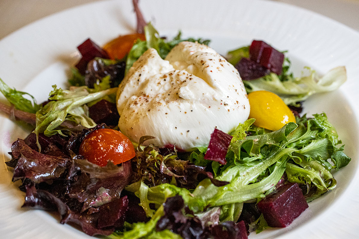 Elegant salad featuring fresh mixed greens, roasted beets, cherry tomatoes, and a perfectly poached egg, served on white china with fresh herbs and microgreens