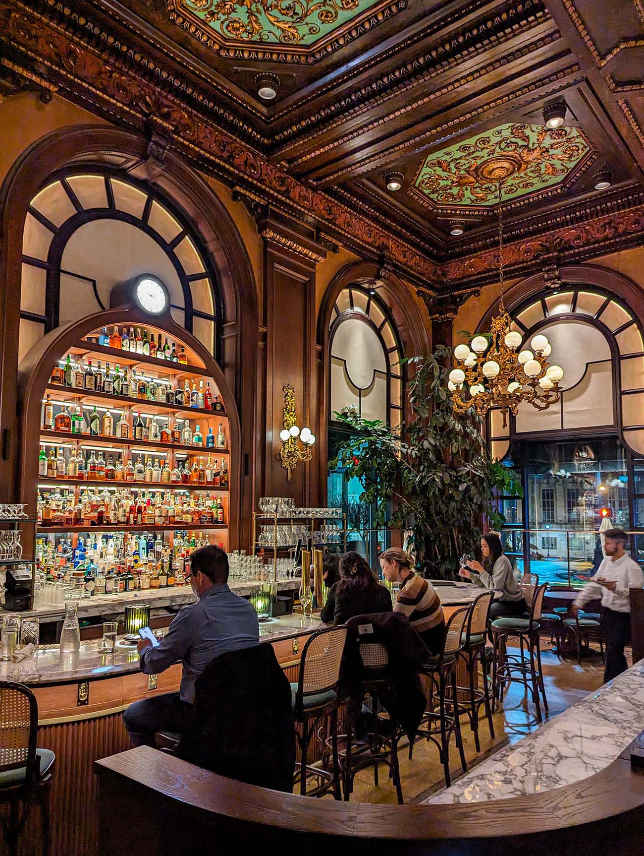 Interior of the ornate Le cavalier bar featuring a vaulted ceiling with intricate gold and green painted medallions, crystal chandeliers, arched windows, and a well-stocked backlit bar - showcasing the "old-world charm and contemporary sophistication" mentioned in the article.