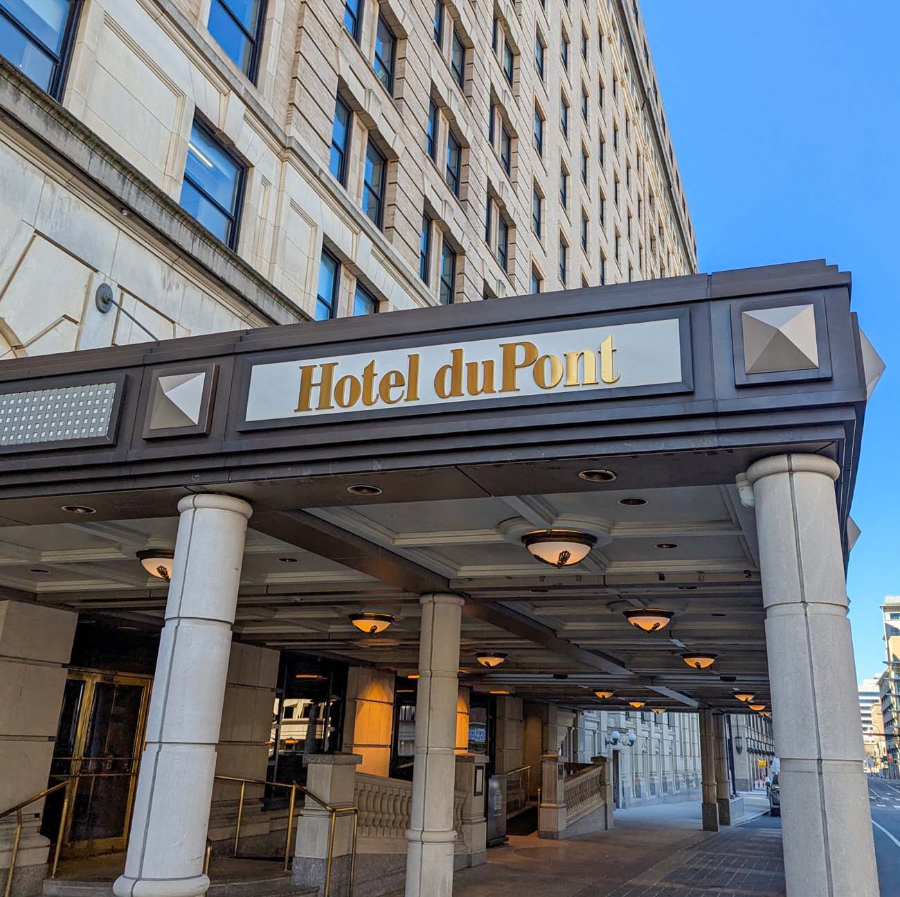 Exterior view of Hotel Du Pont showing the limestone facade, entrance canopy with gold "Hotel duPont" lettering, and classical columns - the historic hotel that opened in 1913 and has hosted celebrities and dignitaries for over a century.