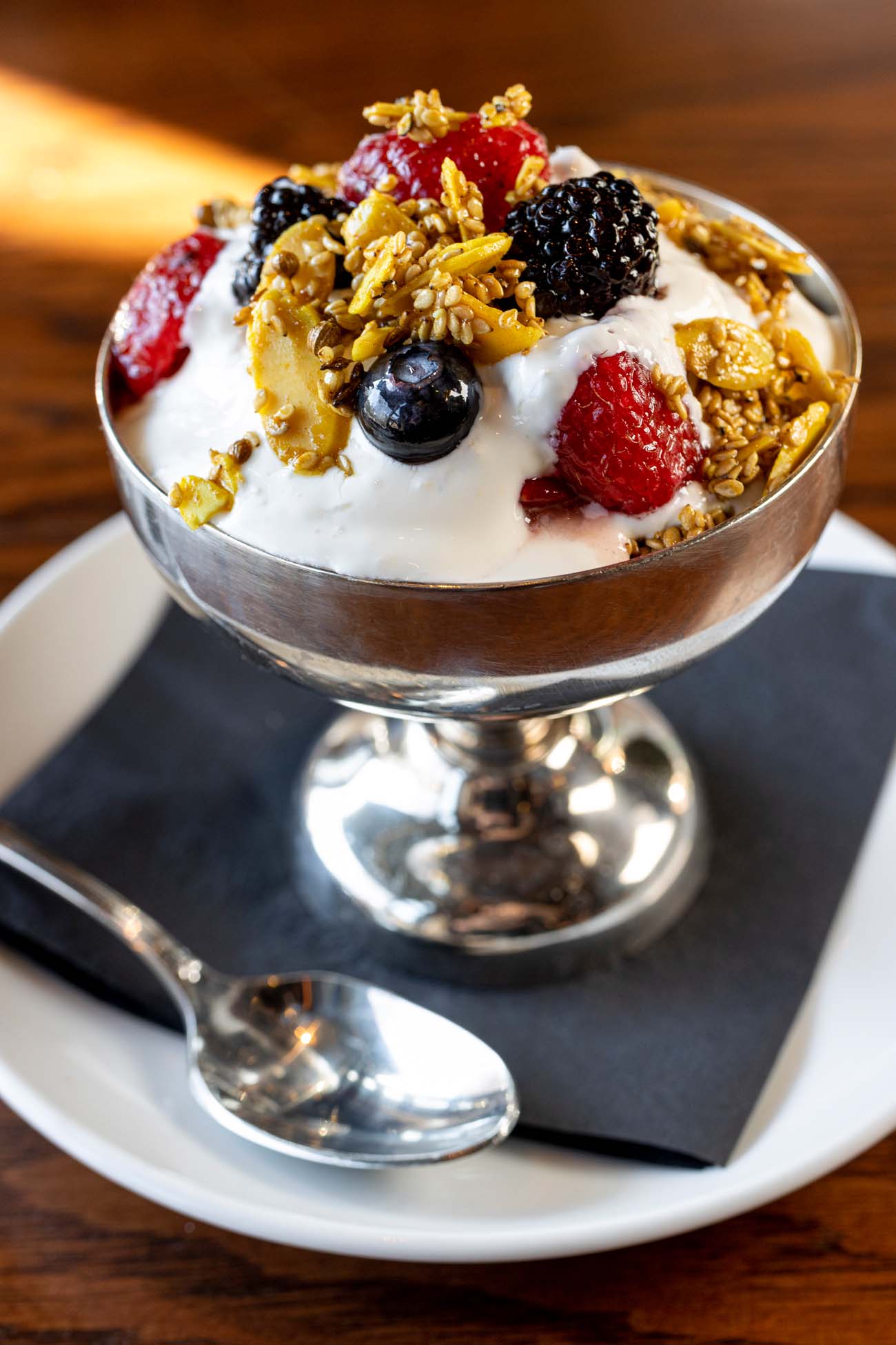 An elegant silver coupe glass filled with labneh parfait topped with fresh berries and candied almond dukkah, exactly as described in the article as "a visual masterpiece served in an elegant silver coupe glass" at Le Cavalier.