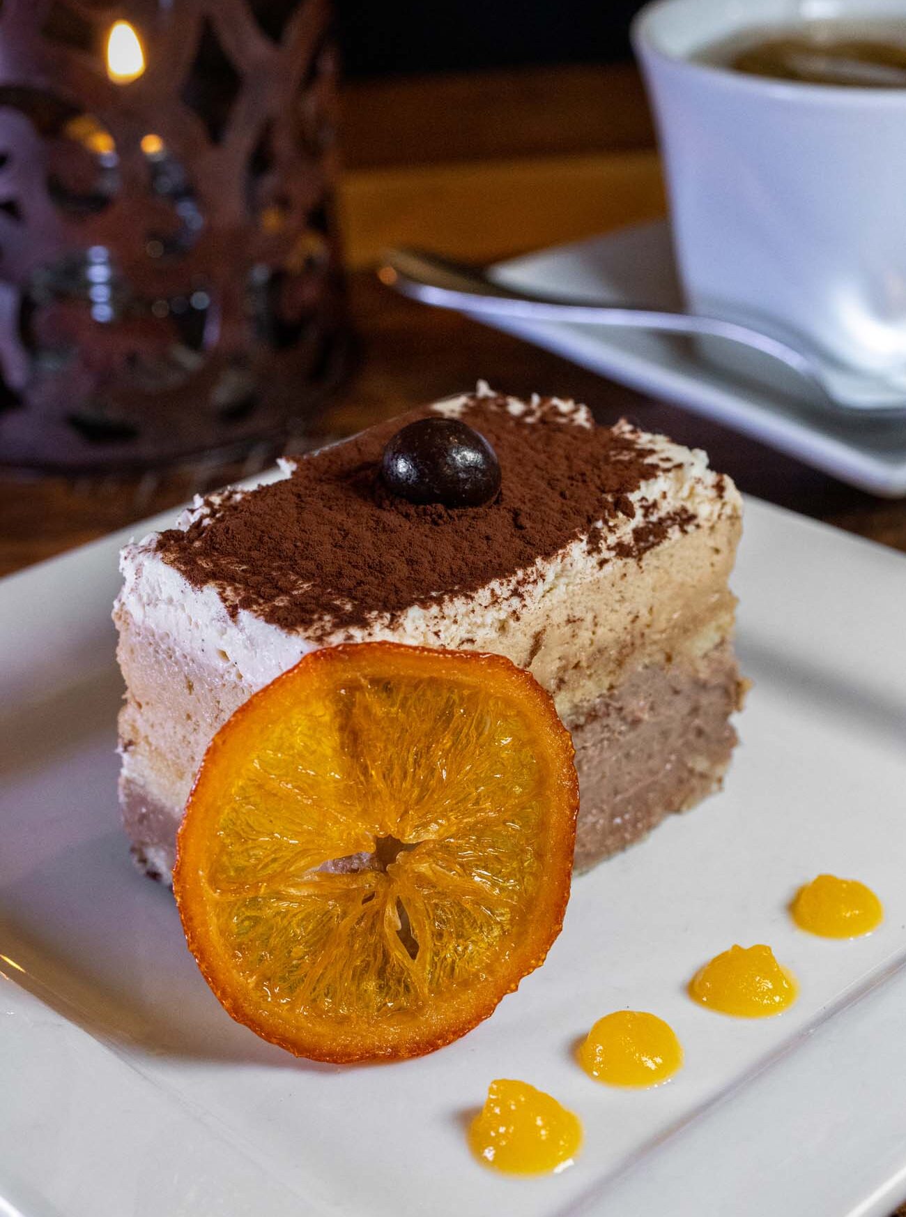 Orange Espresso Torte cake with a candied orange slice. A cup of tea and candle in the background.