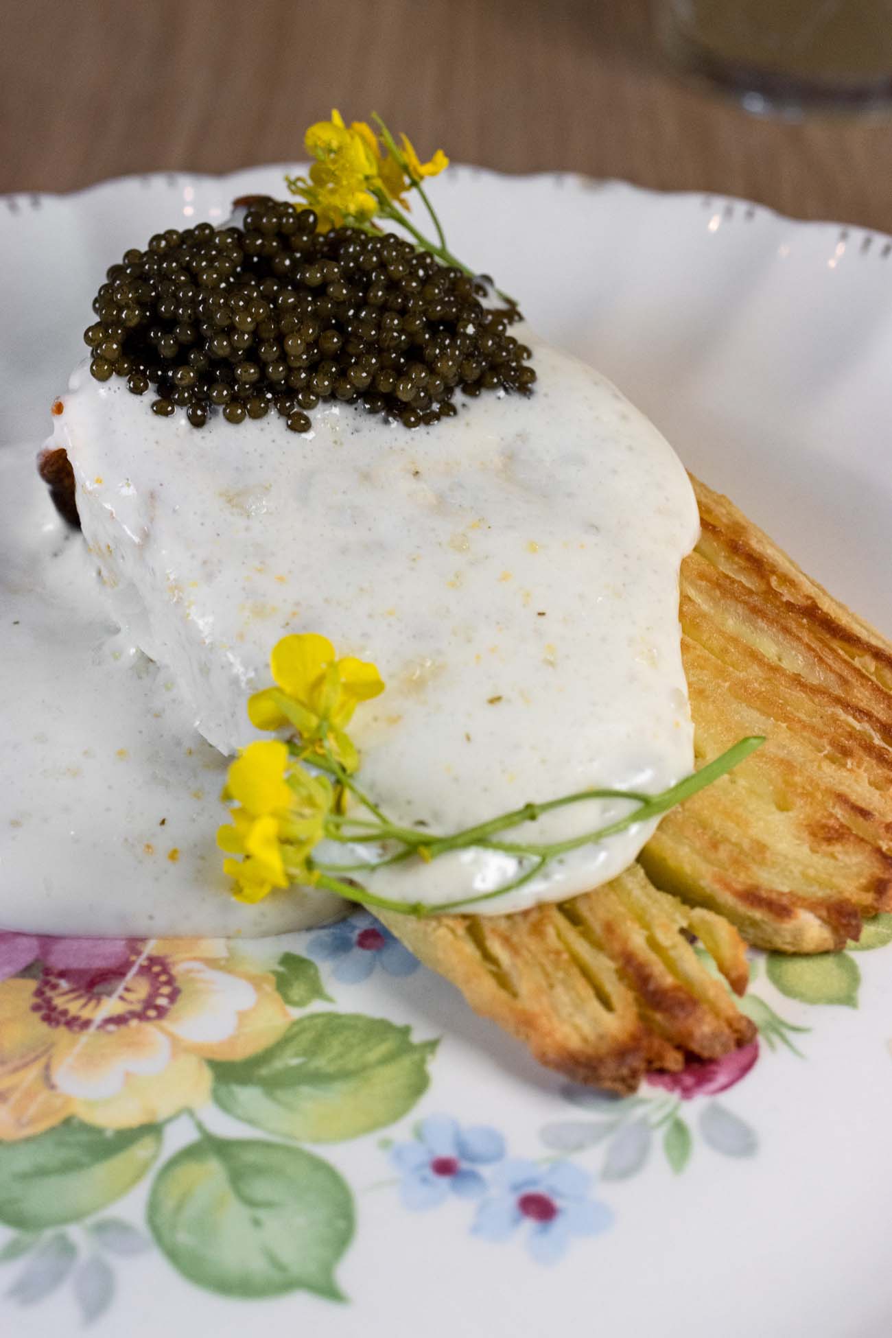 An elegant white plate with a stack of thin green crepes layered with white ricotta, topped with a generous mound of dark caviar, yellow fennel flowers, fresh dill, and delicate microgreens, showcasing Passerine's refined vegetable-forward cuisine