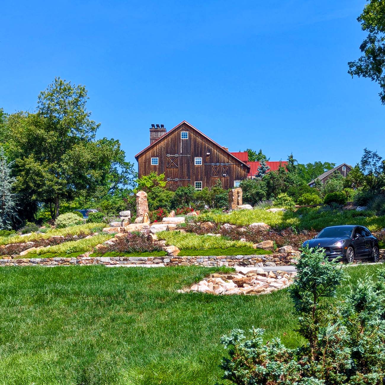 Meticulously maintained terraced landscape featuring natural stone retaining walls, ornamental plantings, and wide lawn areas leading up to the historic barn building in the background