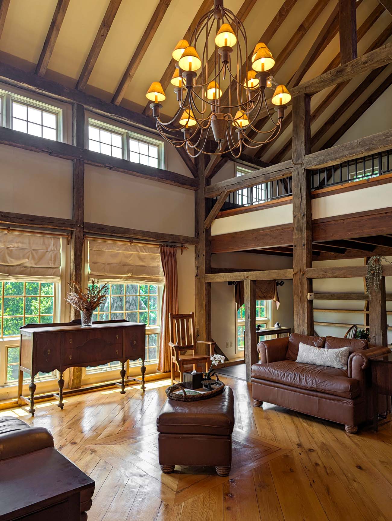 pacious room featuring massive exposed wooden beams, a large wrought iron chandelier, comfortable leather furniture, and a balcony overlooking the living space below