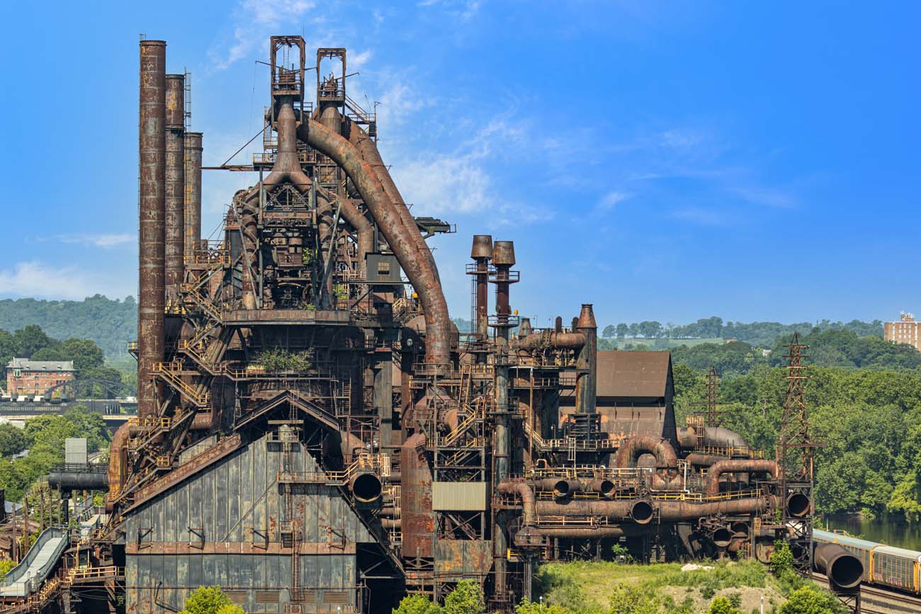 Panoramic view of Bethlehem Steel's historic blast furnaces and industrial structures rising above green hills under blue sky, showcasing the area's industrial heritage