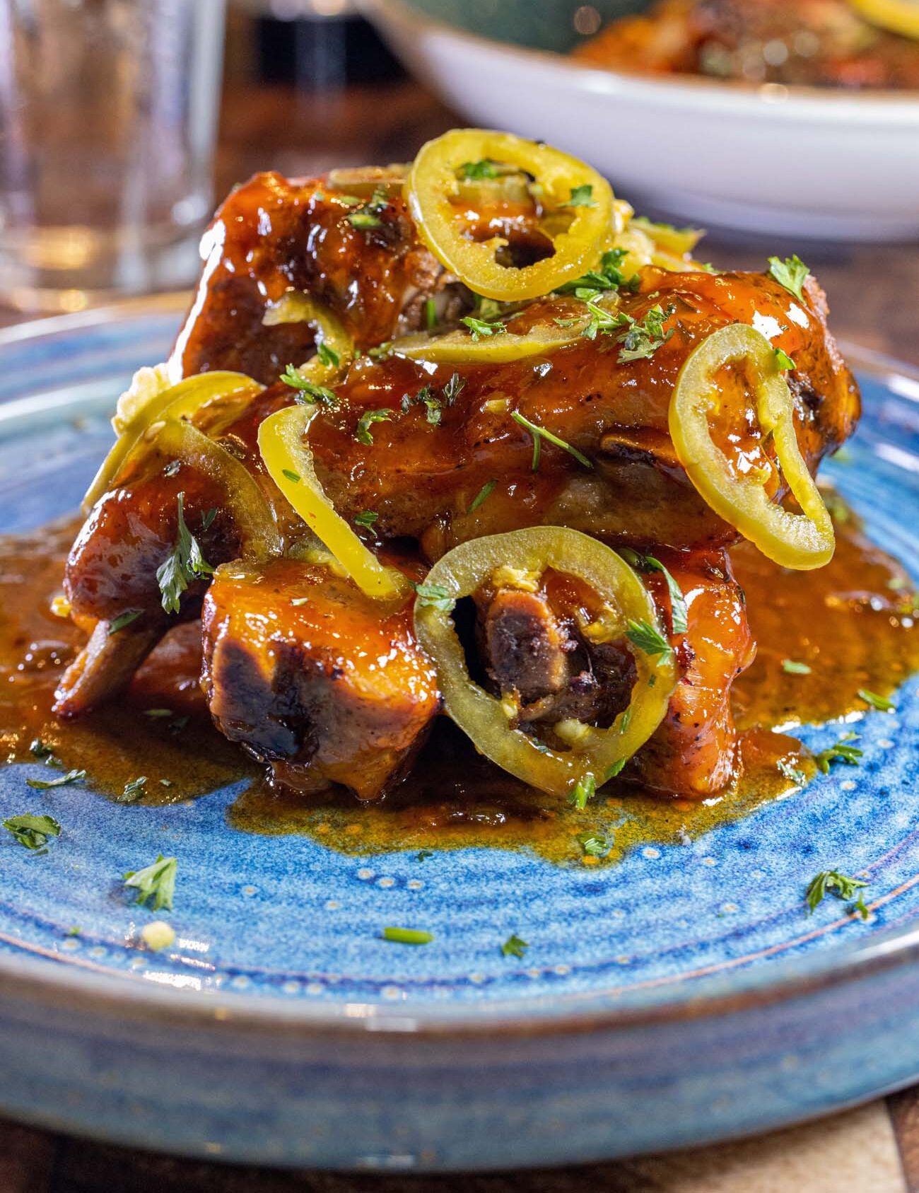 Sweet and spicy grilled baby back ribs with sliced jalapeño peppers and fresh herbs on blue ceramic plate, showcasing the restaurant's elevated comfort food