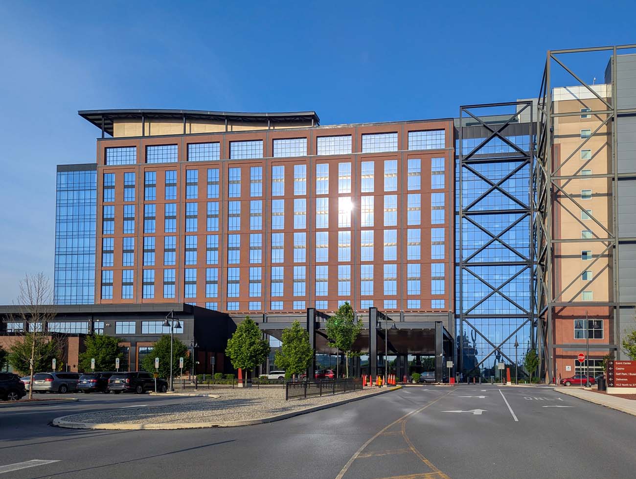 Modern Wind Creek Bethlehem resort exterior showing red hotel tower with glass windows, industrial steel framework, curved entrance canopy, and landscaped approach road