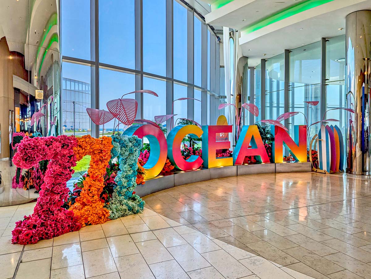 Large colorful "OCEAN" letters display with number 7, surrounded by tropical flowers and beach umbrellas in hotel lobby