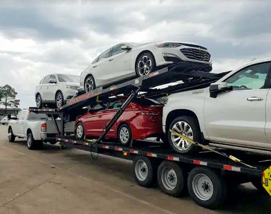 Professional auto transport carrier truck loaded with multiple vehicles including white SUVs and sedans, showing the secure loading system used for cross-country vehicle shipping