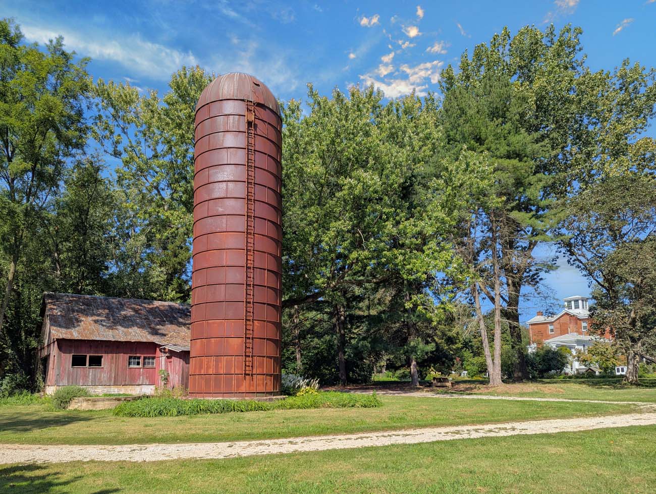 Brampton 1860 Review: A Timeless Retreat on the Eastern Shore 46 A weathered red barn and tall cylindrical silo on Brampton 1860's property, with the historic Manor House visible in the background, showcasing the estate's agricultural heritage.