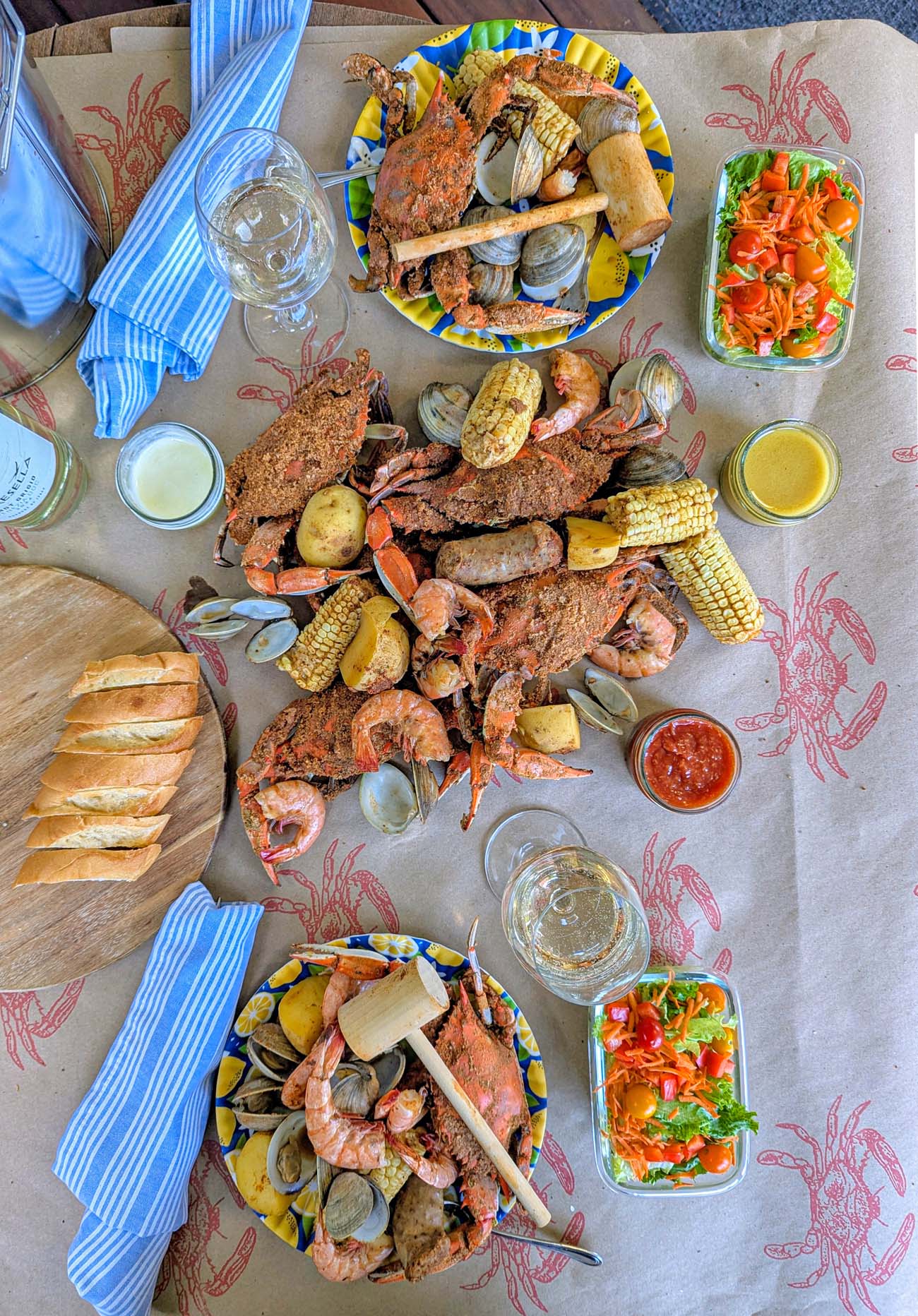 Brampton 1860 Review: A Timeless Retreat on the Eastern Shore 22 Brampton's Signature Steampot spread featuring local crabs, shrimp, clams, corn, potatoes, and kielbasa on brown paper with small salads, bread, and wine glasses.