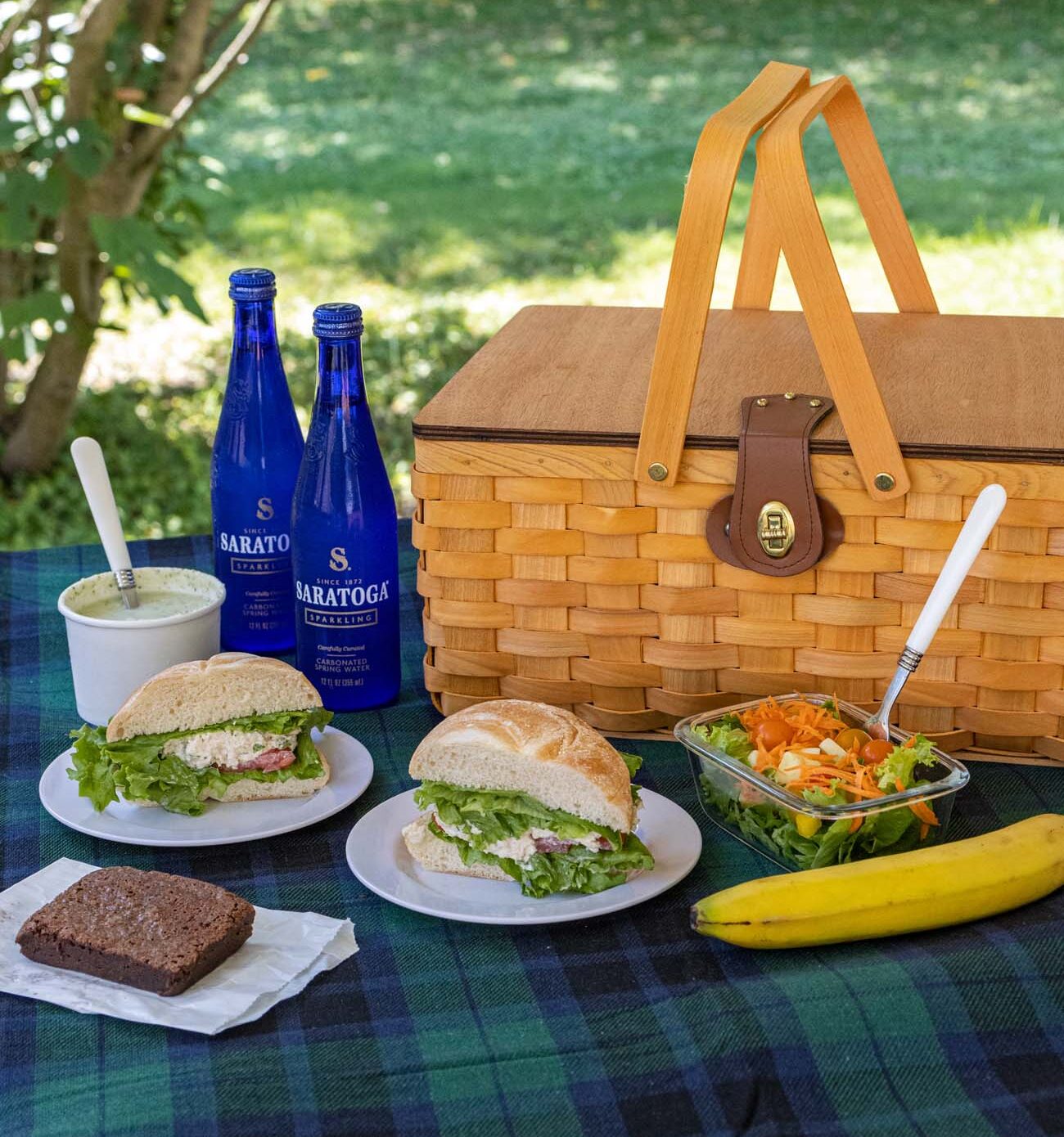 Brampton 1860 Review: A Timeless Retreat on the Eastern Shore 18 A gourmet picnic basket with Carole's chicken salad sandwiches, fresh salads, brownies, fruit, and Saratoga sparkling water arranged on a checkered blanket under trees.