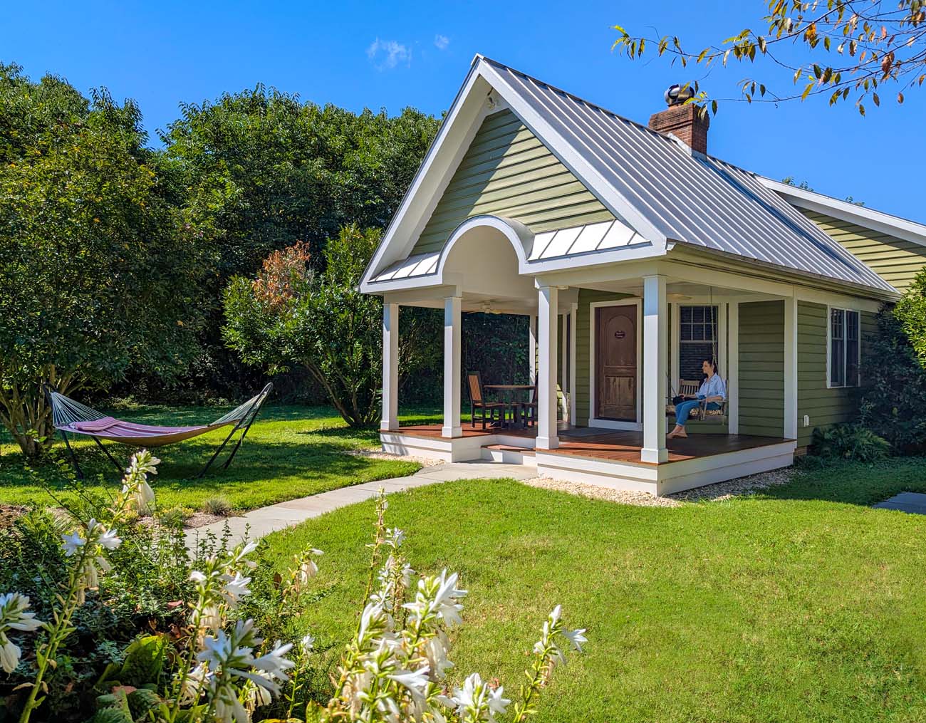 Brampton 1860 Review: A Timeless Retreat on the Eastern Shore 4 The full exterior of Marley's Cottage at Brampton 1860, showing the sage green cottage with white trim, covered porch, and hammock, surrounded by lush lawns and gardens.