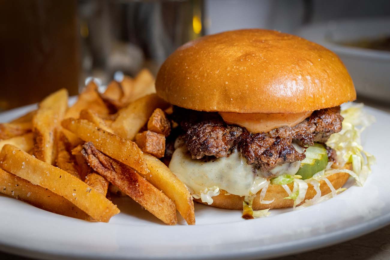 Food, Wine, and Fall Fun at Brampton 1860 - Chestertown, MD 14 hick burger with melted cheese on brioche bun with lettuce and special sauce, served with generous portion of golden french fries on white plate, restaurant setting