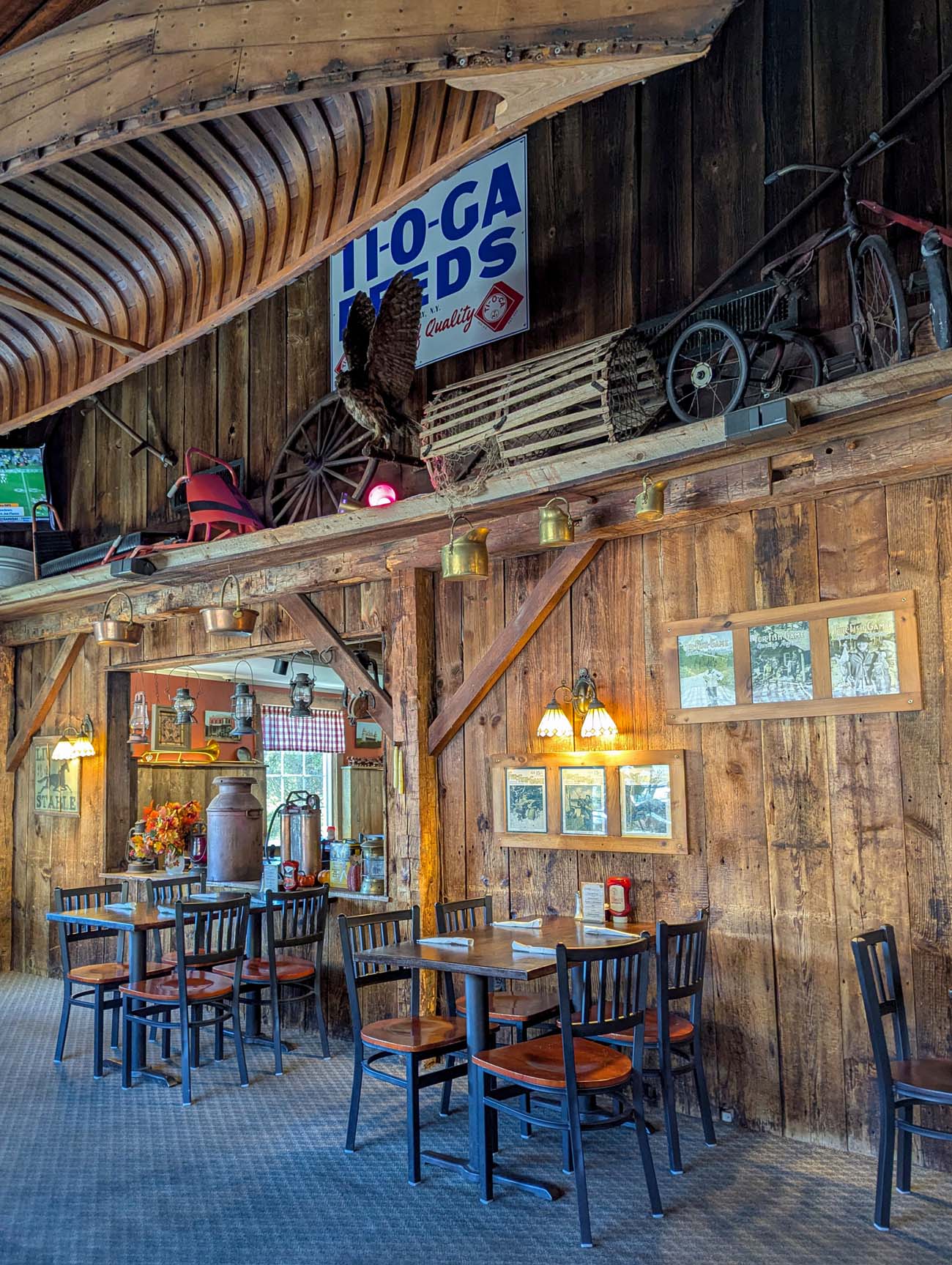 Rustic barn interior at Apple Valley Restaurant showing exposed wooden beams, vintage Ito-Ga Feeds sign, antique wagon wheels, and cozy dining tables in Milford Pike County Pennsylvania