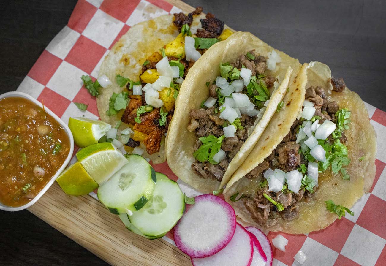 Things to Do in Chestertown MD: Eastern Shore Travel Guide 24 Three authentic Mexican street tacos on warm corn tortillas with seasoned meat, diced onions and fresh cilantro on red and white checkered paper, served with cucumber slices, radish, lime wedges and small bowl of salsa verde on wooden board