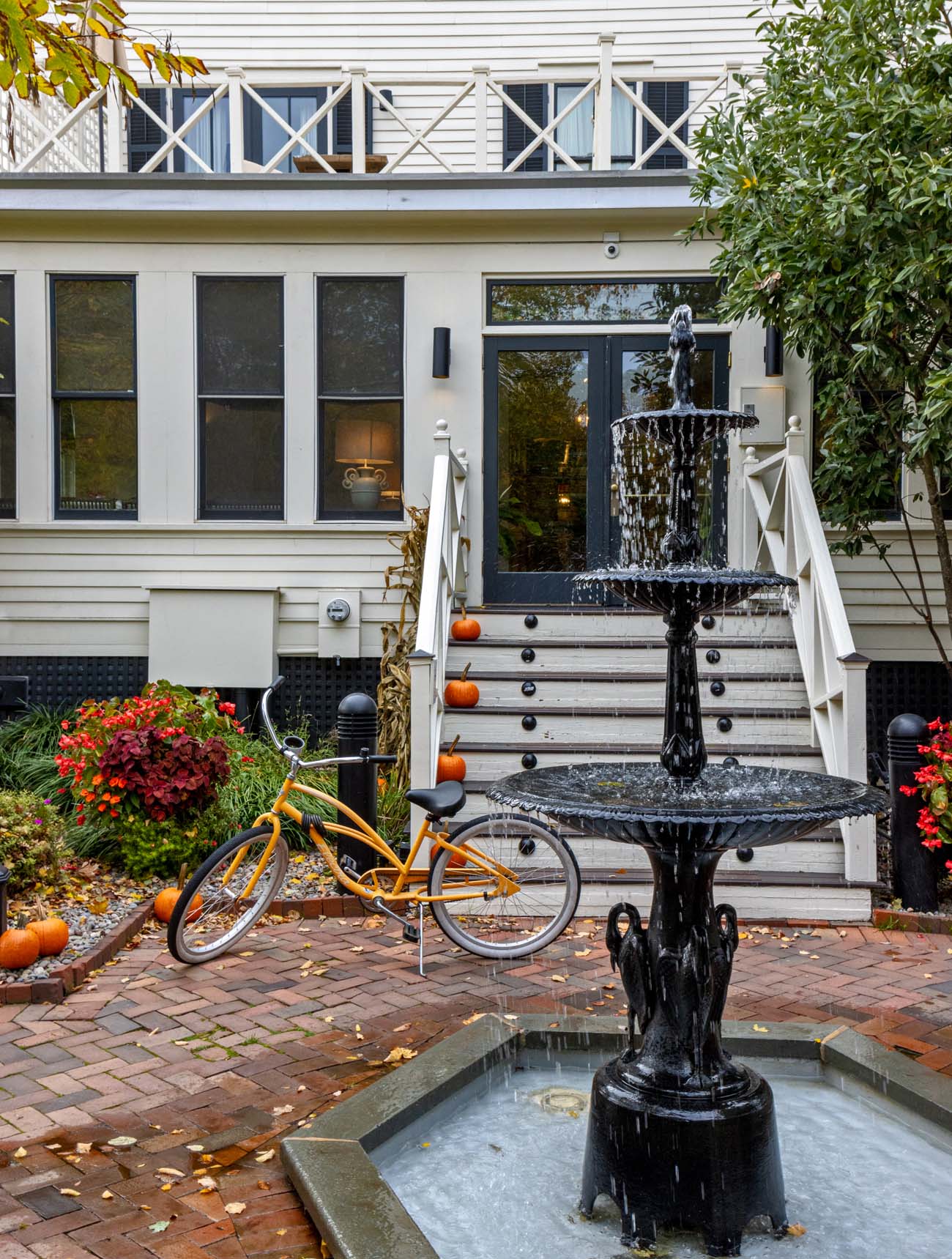 Serene garden courtyard at historic Hotel Fauchere featuring ornate black Victorian fountain with flowing water, fall flowers, pumpkin decorations, yellow vintage beach cruiser bicycle for guests in downtown Milford Pennsylvania