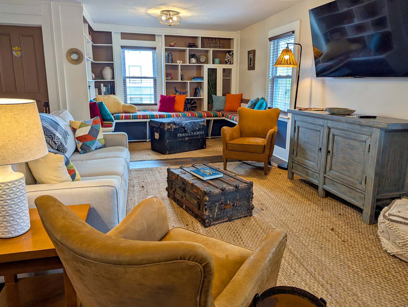 Spacious Presidential Suite living room at La Posada boutique Mexican inn featuring colorful built-in window seat with vibrant pillows, vintage steamer trunks, mustard yellow leather chairs, sisal rug and eclectic decor in Milford Pike County Pennsylvania