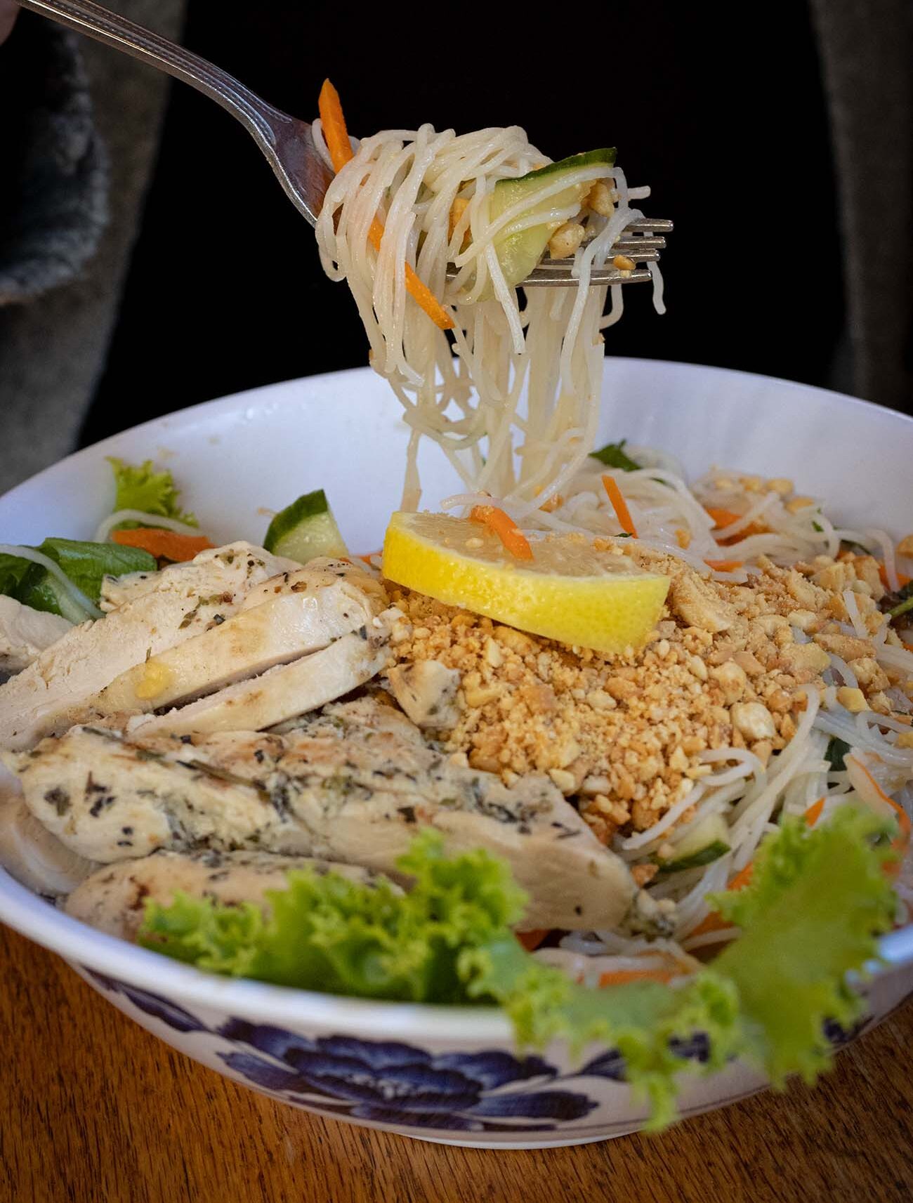 Vietnamese rice noodle salad bowl with sliced grilled herb chicken breast, fresh cucumber slices, julienned carrots, crispy crushed peanuts, fresh lemon wedge and lettuce being twirled on fork showing noodle texture at The Waterwheel Cafe bakery bar in restored 19th century grist mill listed on National Register of Historic Places Milford Pike County Pennsylvania Pocono Mountains