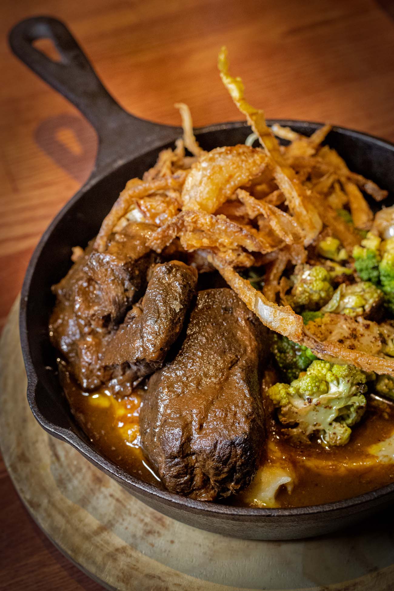 Sixty hour braised beef short ribs with creamy mashed potatoes, roasted Romanesco cauliflower, red wine demi glaze and crispy fried shallot strings served in cast iron skillet at historic Tom Quick Inn 1800s Victorian tavern in downtown Milford Pike County Pennsylvania