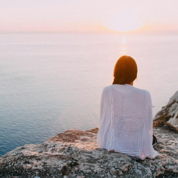 Person sitting peacefully by the ocean at sunset, representing self-reflection and inner peace