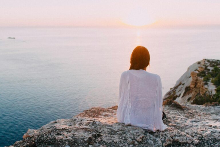 Person sitting peacefully by the ocean at sunset, representing self-reflection and inner peace