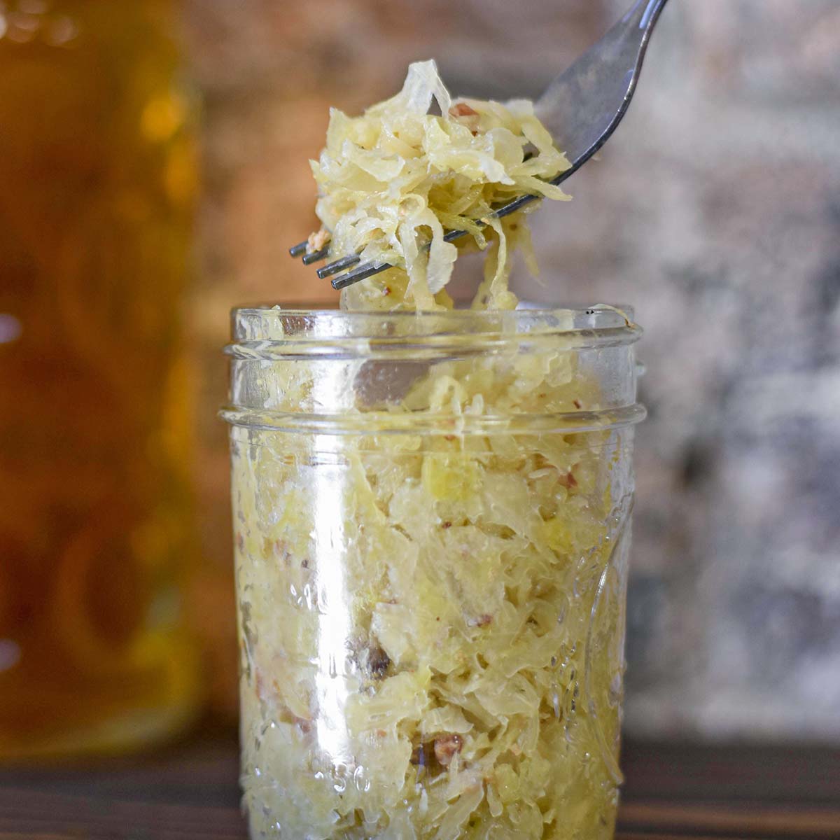 Close-up of fork lifting strands of tangy fermented sauerkraut from clear glass mason jar showing golden-yellow fermented cabbage with visible brine and texture, demonstrating properly fermented homemade sauerkraut with cloudy liquid and crisp shredded cabbage strands
