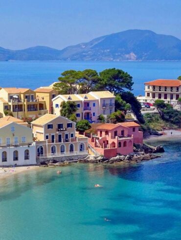An aerial shot of a sunny day on Assos in Greece. Colorful villa style homes with boats in the clear water.