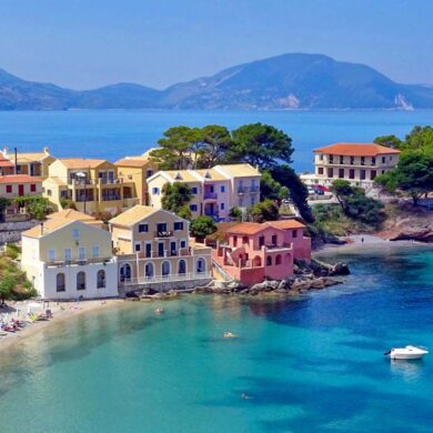 An aerial shot of a sunny day on Assos in Greece. Colorful villa style homes with boats in the clear water.