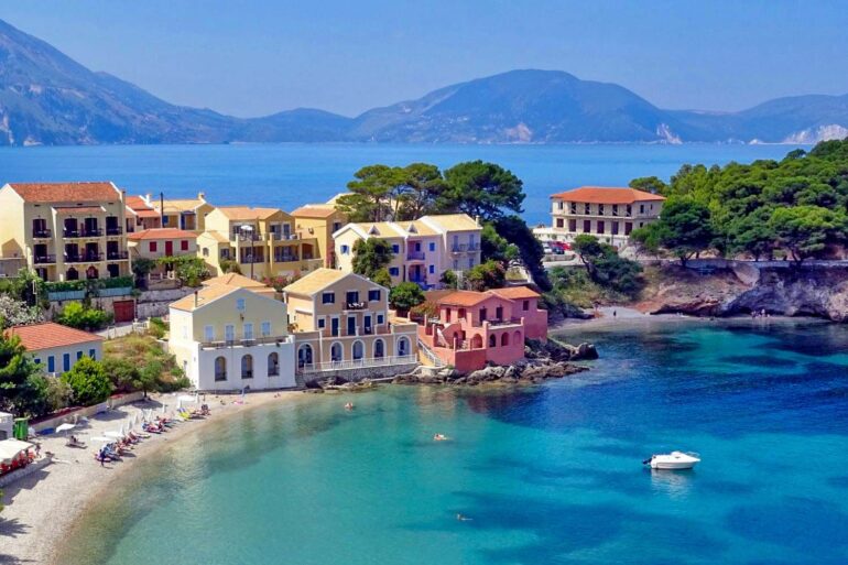 An aerial shot of a sunny day on Assos in Greece. Colorful villa style homes with boats in the clear water.