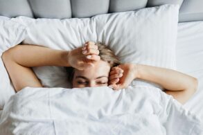 A woman in bed in the early morning. She's just waking up and beginning to stretch.