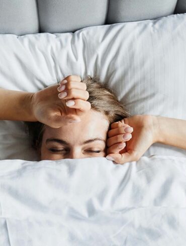 A woman in bed in the early morning. She's just waking up and beginning to stretch.