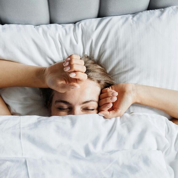 A woman in bed in the early morning. She's just waking up and beginning to stretch.
