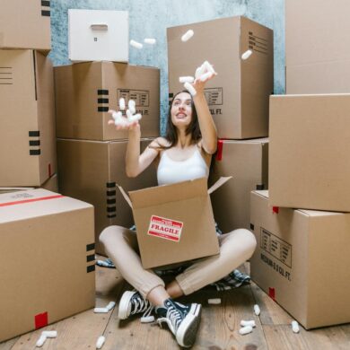 a woman surrounded by moving boxes and throwing packing peanuts into the air