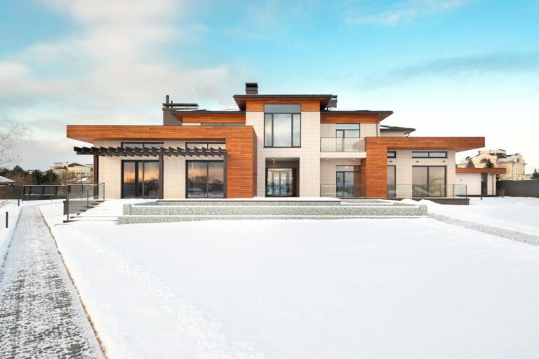 A modern home with large floor to ceiling windows, warm wood cladding, and a clean entryway, surrounded by snow on a bright winter day, showcasing how upgraded glazing and entryways can transform a home's curb appeal.