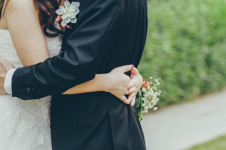 Bride and groom embrace holding white flowers on wedding day, planning an affordable and beautiful stress-free celebration