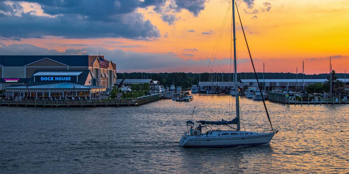 Romantic sunset over Kent Narrows Maryland with sailboat anchored in calm water and waterfront restaurants along the Chesapeake Bay creating intimate atmosphere for couples