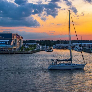Romantic sunset over Kent Narrows Maryland with sailboat anchored in calm water and waterfront restaurants along the Chesapeake Bay creating intimate atmosphere for couples