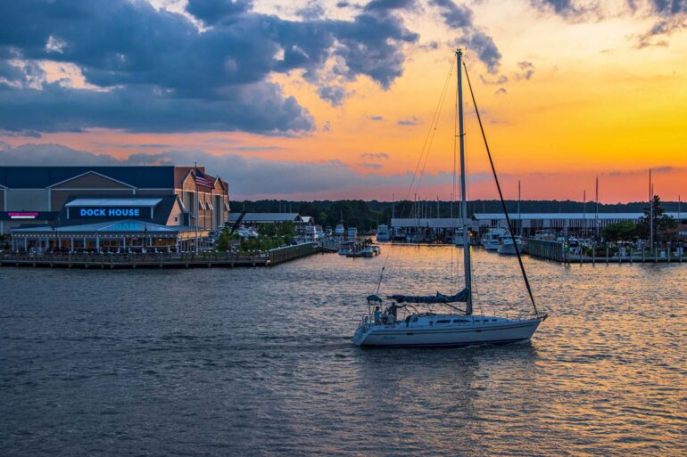 Romantic sunset over Kent Narrows Maryland with sailboat anchored in calm water and waterfront restaurants along the Chesapeake Bay creating intimate atmosphere for couples