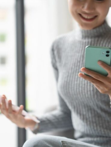 woman on her phone holding a checking account statement and smiling.