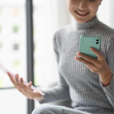 woman on her phone holding a checking account statement and smiling.